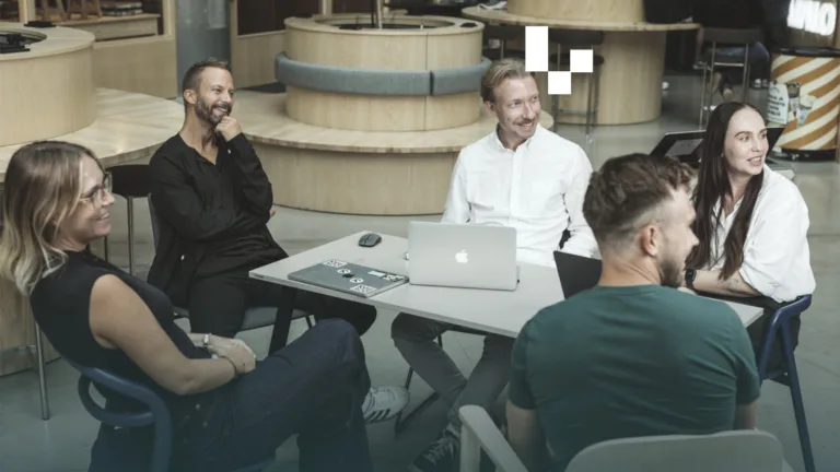 Resaco team members talking around a table with laptops in a bright office